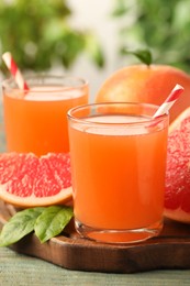 Photo of Glasses of delicious grapefruit juice on wooden table against blurred background