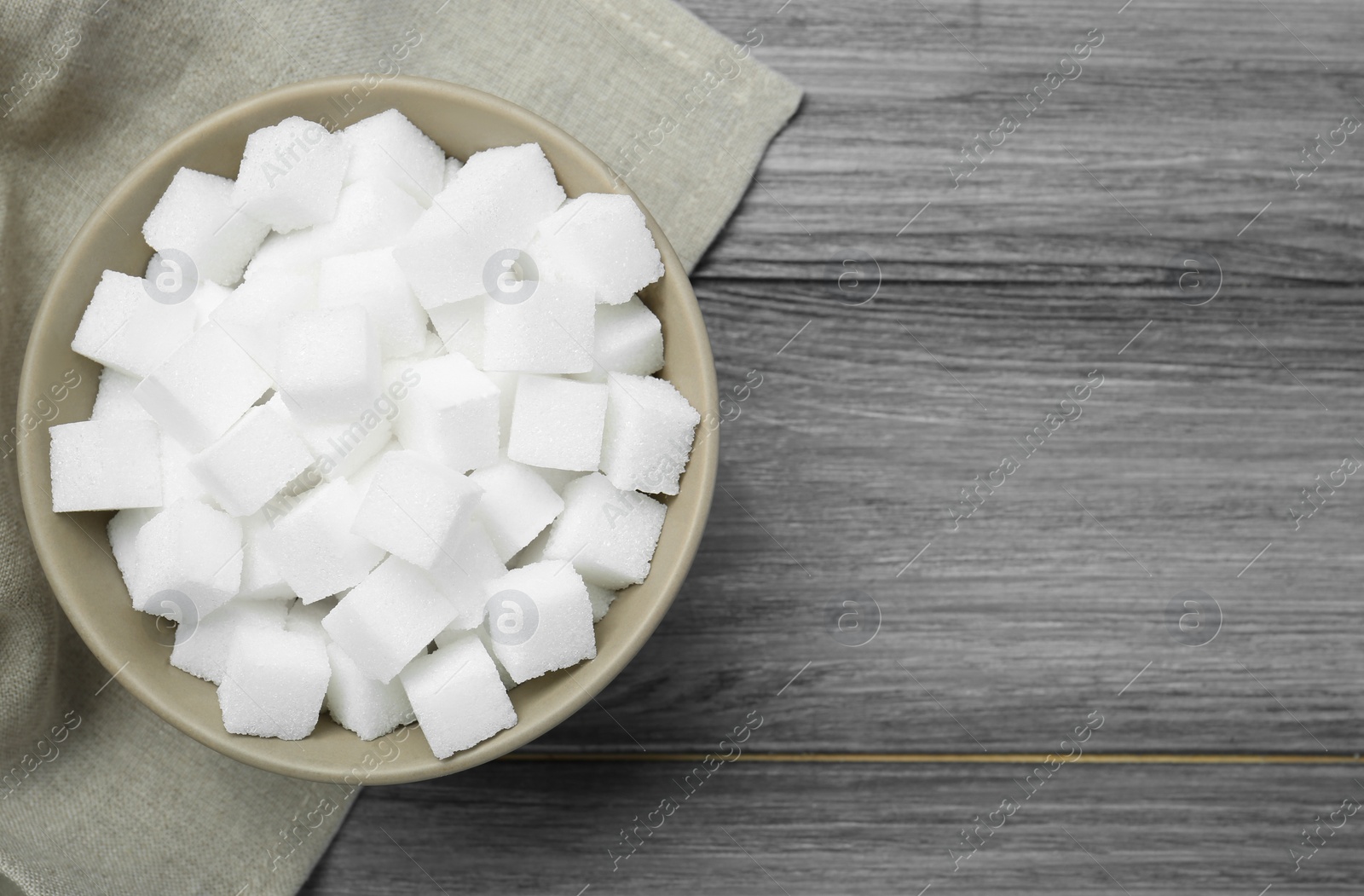 Photo of White sugar cubes in bowl on wooden table, top view. Space for text