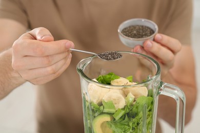 Man adding chia seeds into blender with ingredients for smoothie, closeup