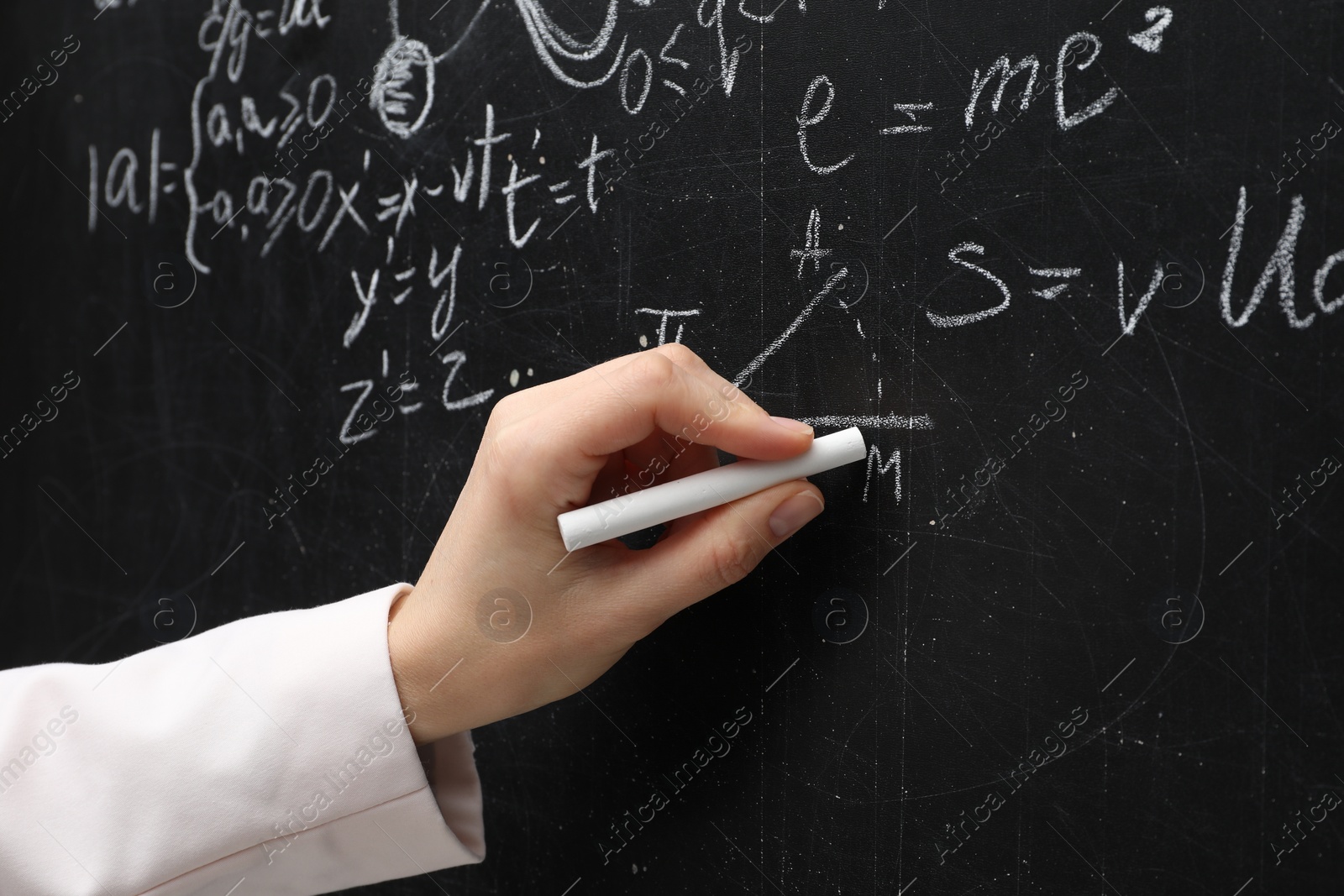 Photo of Teacher writing physical formulas with chalk on black chalkboard, closeup