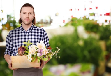 Florist holding basket with flowers in shop. Space for text 