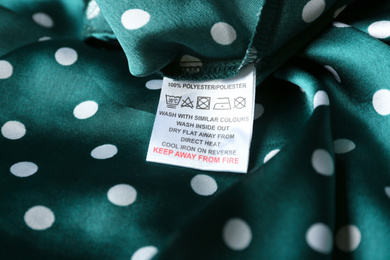 Photo of Clothing label with care instructions and content information on green polka dot garment, closeup