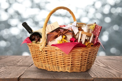 Wicker basket full of gifts on wooden table against blurred festive lights 