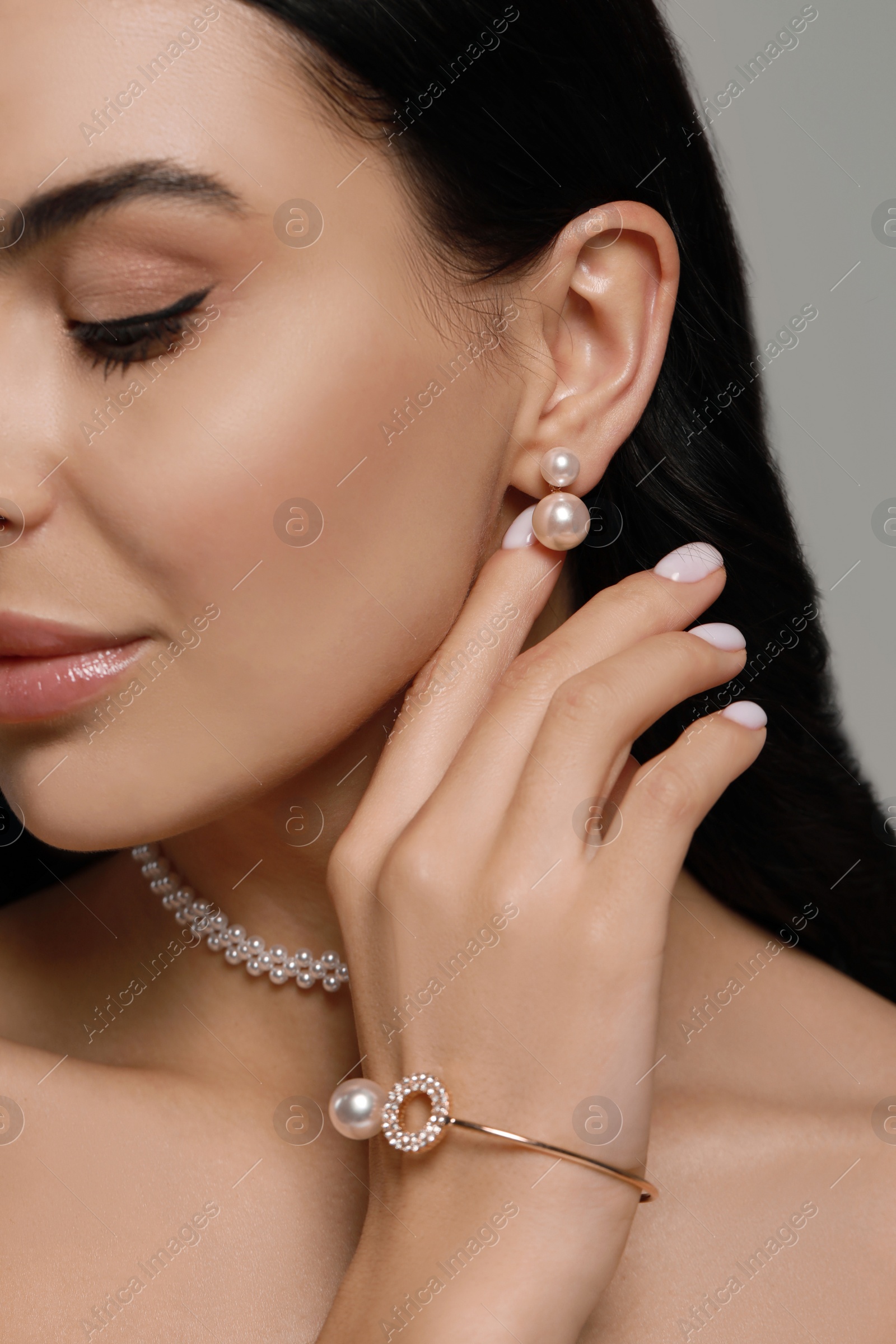 Photo of Young woman wearing elegant pearl jewelry on grey background, closeup