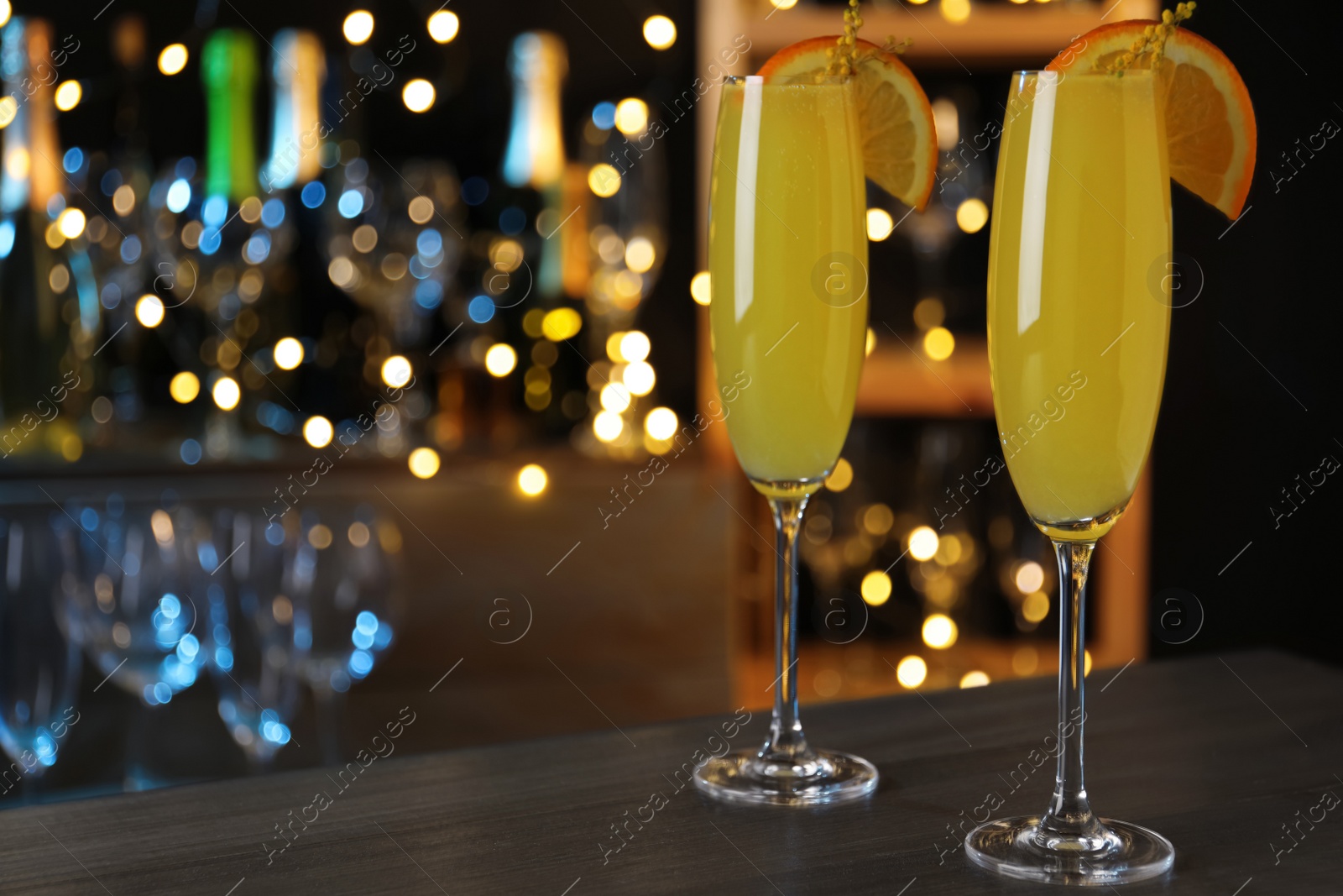 Photo of Mimosa cocktail with garnish on bar counter against blurred lights, space for text