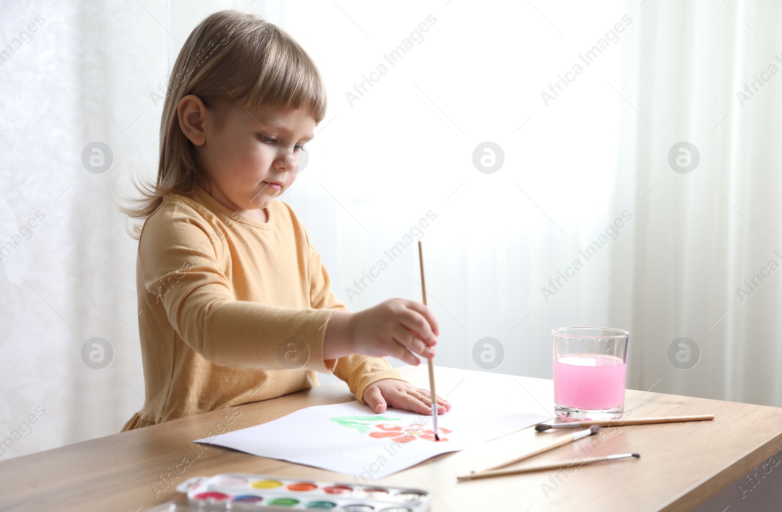 Photo of Cute little girl drawing with brush at wooden table indoors. Child`s art