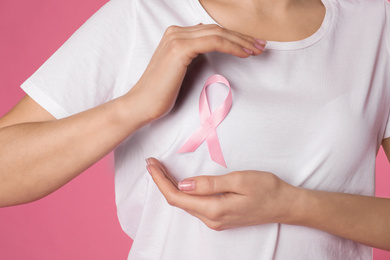 Woman with pink ribbon on color background, closeup. Breast cancer awareness