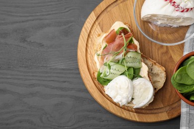 Photo of Tasty sandwich with burrata cheese, prosciutto, cucumber and ingredients on grey wooden table, flat lay. Space for text