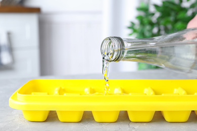 Photo of Pouring water into ice cube tray on table, closeup