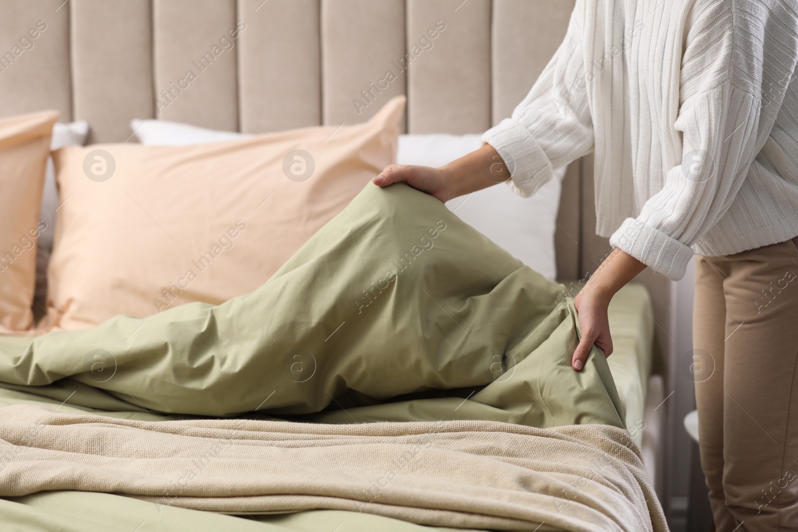 Photo of Woman making bed with new pistachio linen in room, closeup