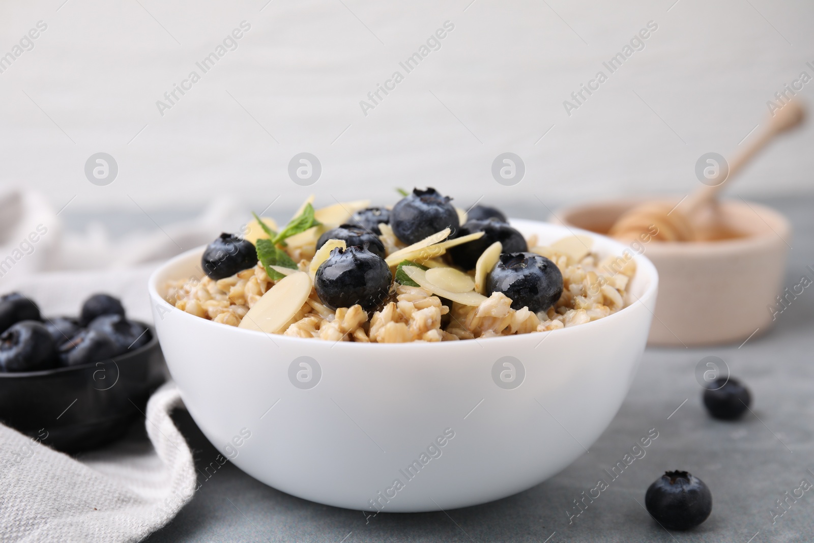 Photo of Tasty oatmeal with blueberries, mint and almond petals in bowl on grey table, closeup