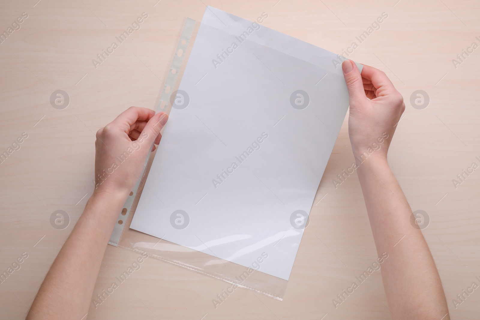 Photo of Woman holding punched pocket with paper sheet at wooden table, top view