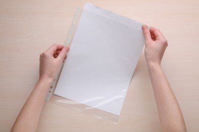 Photo of Woman holding punched pocket with paper sheet at wooden table, top view