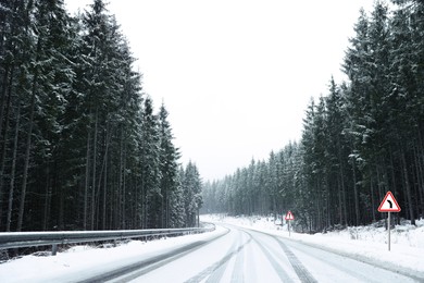 Image of Traffic signs BEND TO LEFT and DANGER near snowy road going through coniferous forest in winter