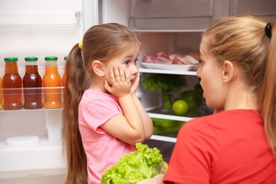 Photo of Emotional young mother and daughter near refrigerator at home