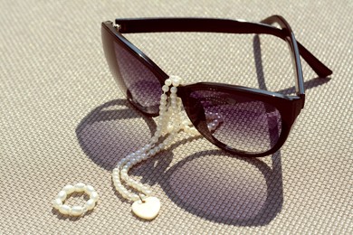 Stylish sunglasses and jewelry on grey surface, closeup