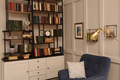 Photo of Cozy home library interior with collection of different books on shelves and comfortable place for reading