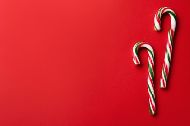 Photo of Delicious Christmas candy canes on red background, flat lay. Space for text