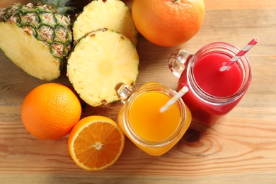 Flat lay composition with different juices in mason jars and fresh fruits on wooden table