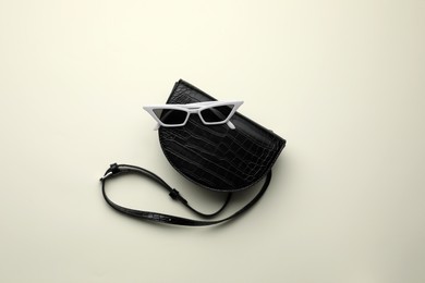 Photo of Stylish woman's bag and sunglasses on light background, top view