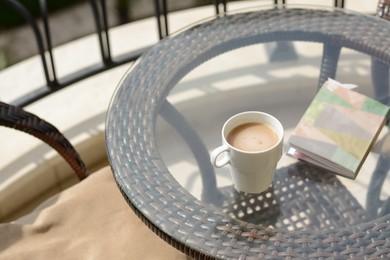 Photo of Ceramic cup of drink and notebook with pen on glass table outdoors. Good morning