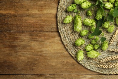 Photo of Wicker mat with fresh green hops and wheat ears on wooden table, top view. Space for text