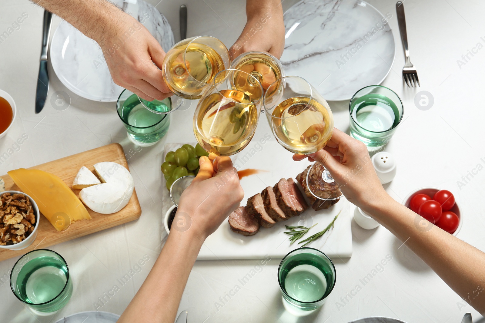 Photo of People holding glasses of white wine over table with tasty snacks, above view