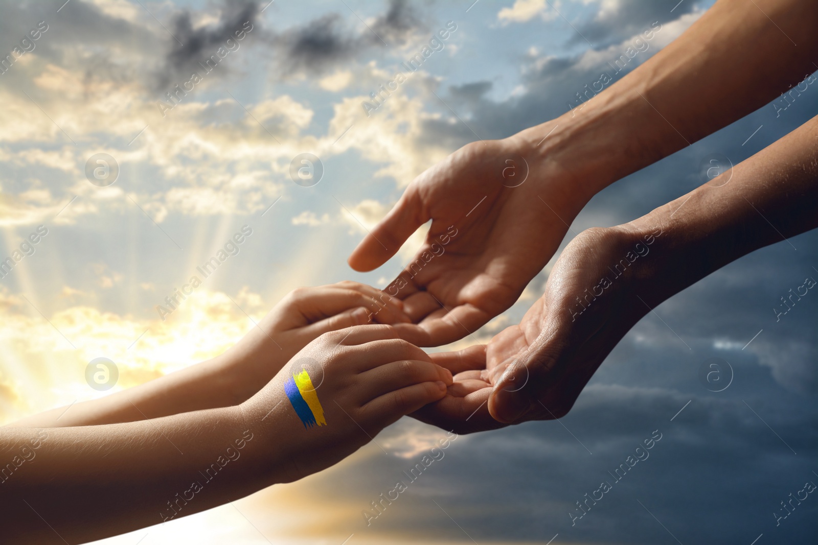 Image of Help for Ukraine. People holding hands with drawing of Ukrainian flag and beautiful sky with clouds at sunset on background, closeup