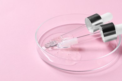 Photo of Pipettes and petri dish with serum sample on pink background, closeup. Space for text