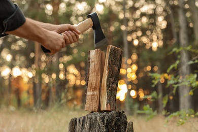 Photo of Man splitting firewood with axe in forest, closeup