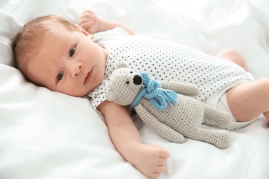 Adorable newborn baby with toy lying on bed sheet