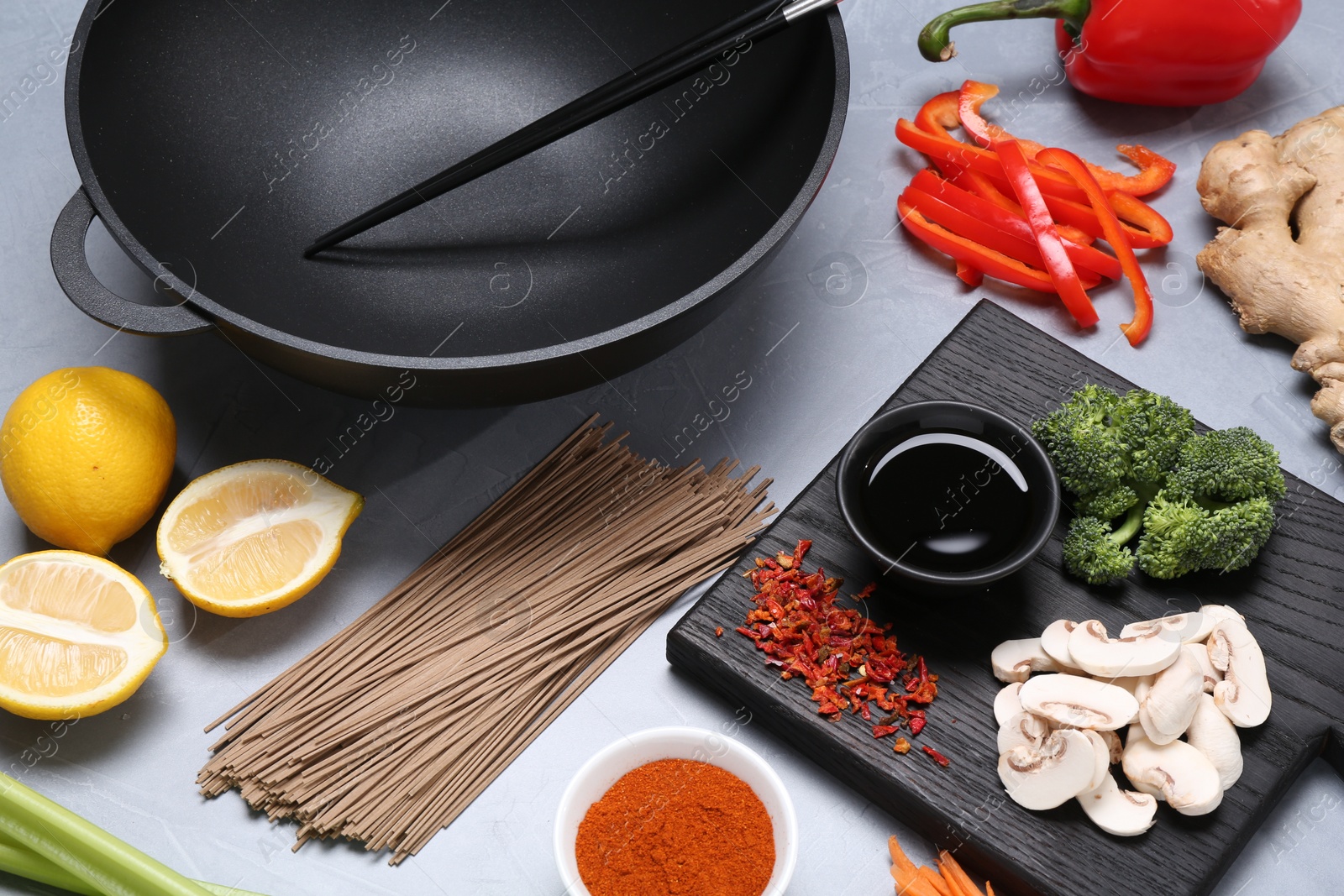 Photo of Wok, chopsticks and different products on grey table, closeup