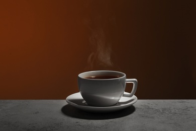 Photo of Ceramic cup of hot fresh tea on stone table against brown background, space for text