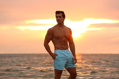 Photo of Handsome young man posing on beach near sea at sunset