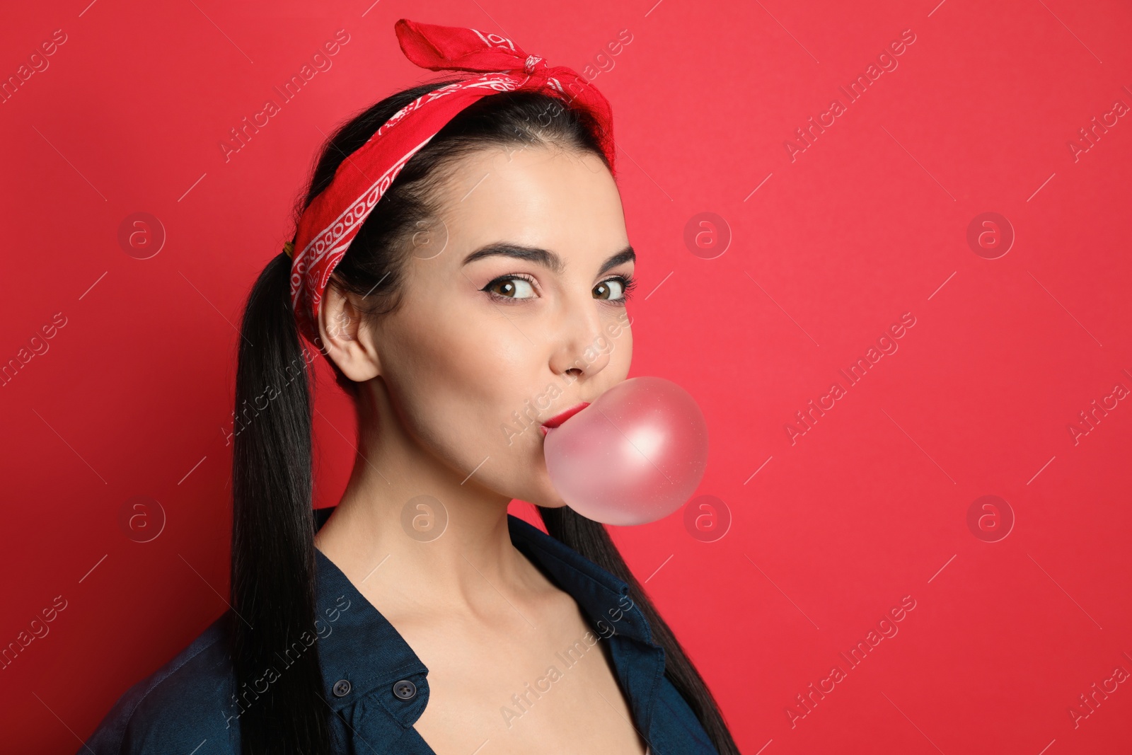 Photo of Fashionable young woman in pin up outfit blowing bubblegum on red background, space for text