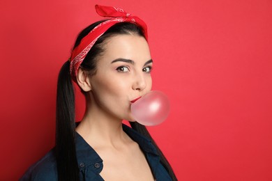 Fashionable young woman in pin up outfit blowing bubblegum on red background, space for text