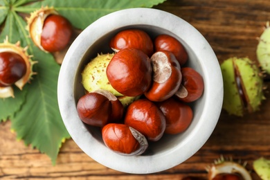 Photo of Horse chestnuts in bowl on wooden table, top view