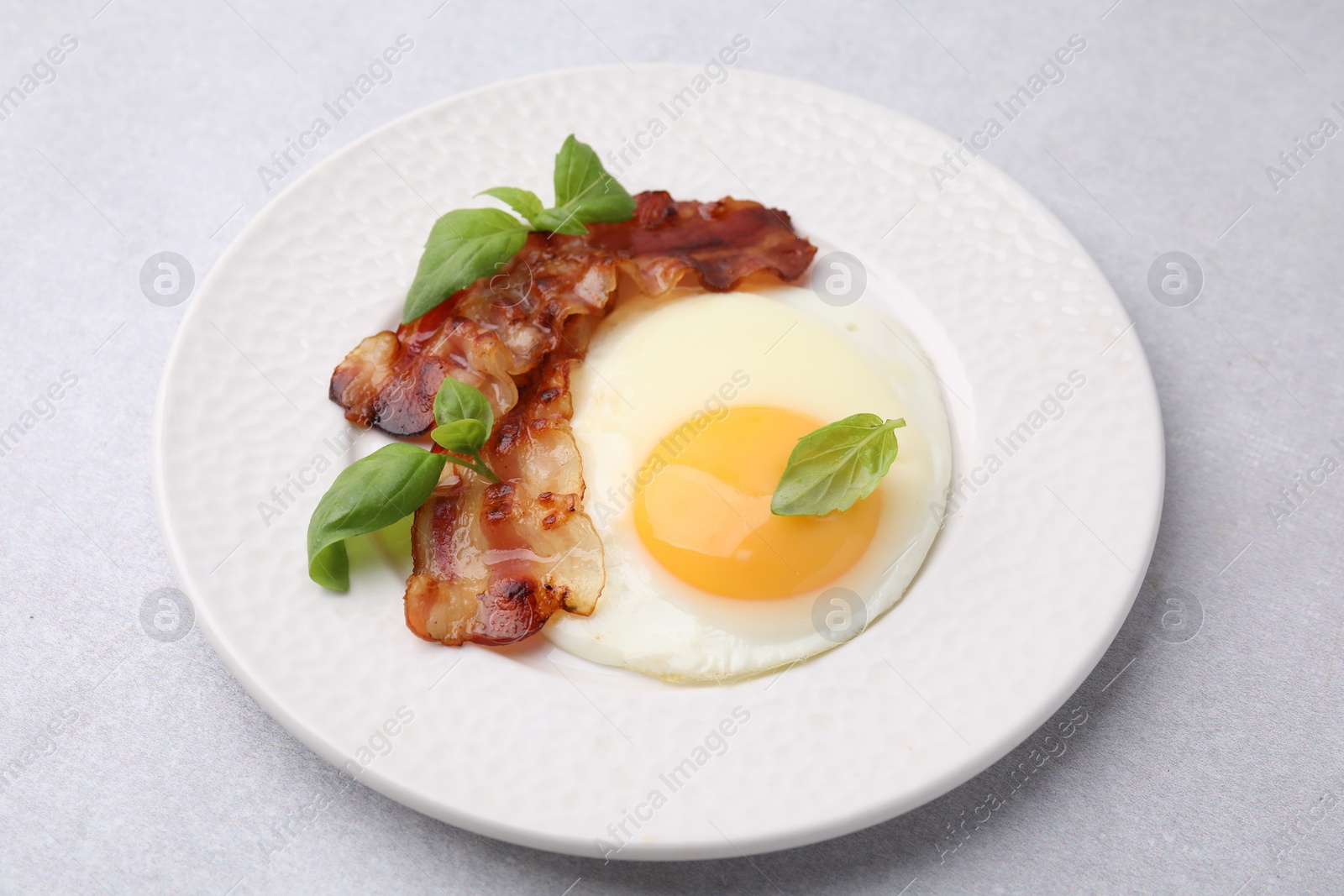 Photo of Fried egg, bacon and basil on light grey table