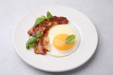 Fried egg, bacon and basil on light grey table