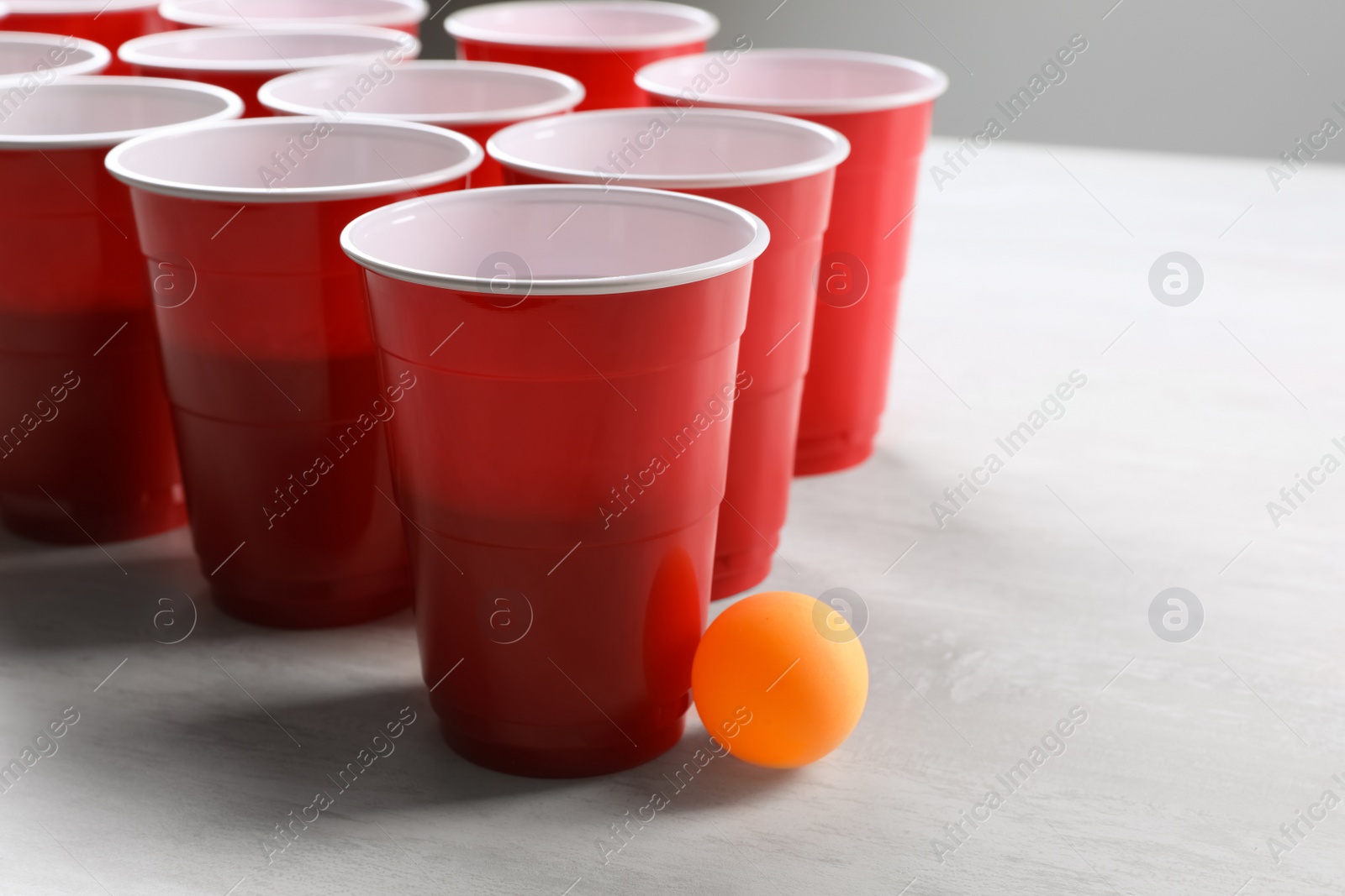 Photo of Plastic cups and ball on white table, space for text. Beer pong game