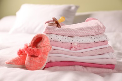 Stack of baby girl's clothes, pacifier and shoes on bed