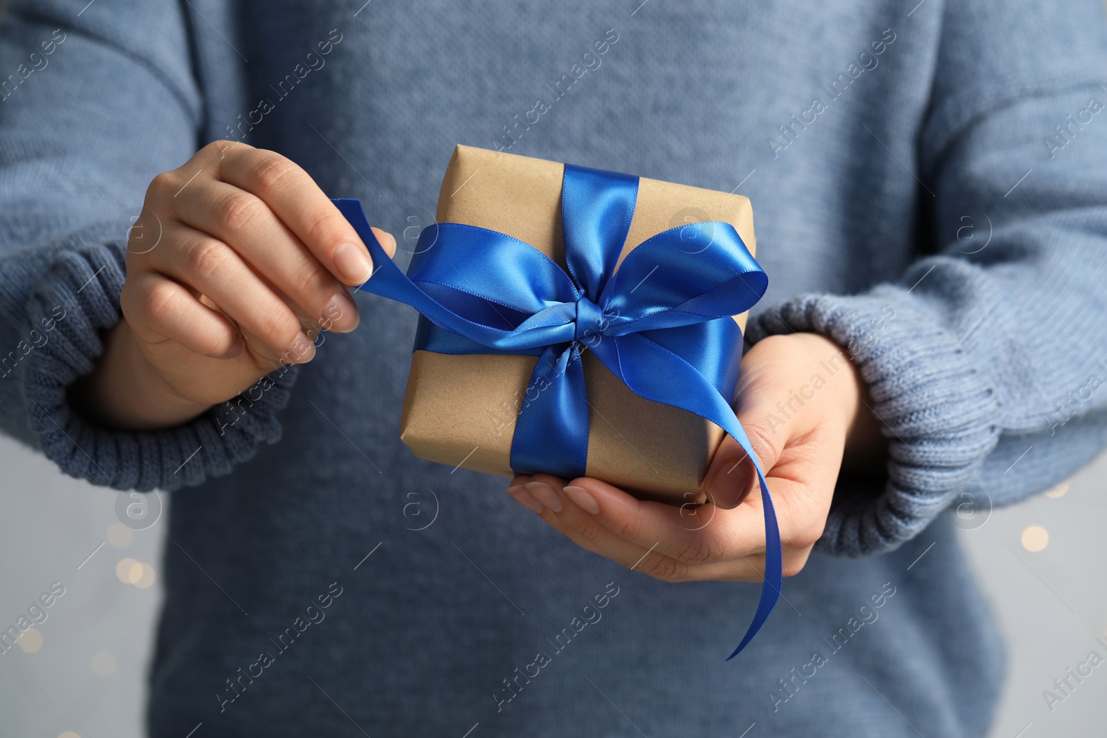 Photo of Woman holding gift box with blue bow on light grey background, closeup