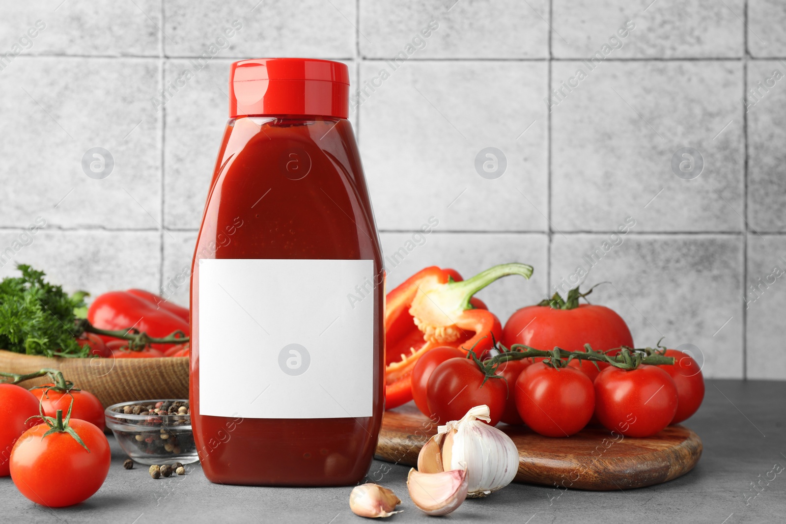 Photo of Bottle of tasty ketchup and ingredients on grey table. Space for text