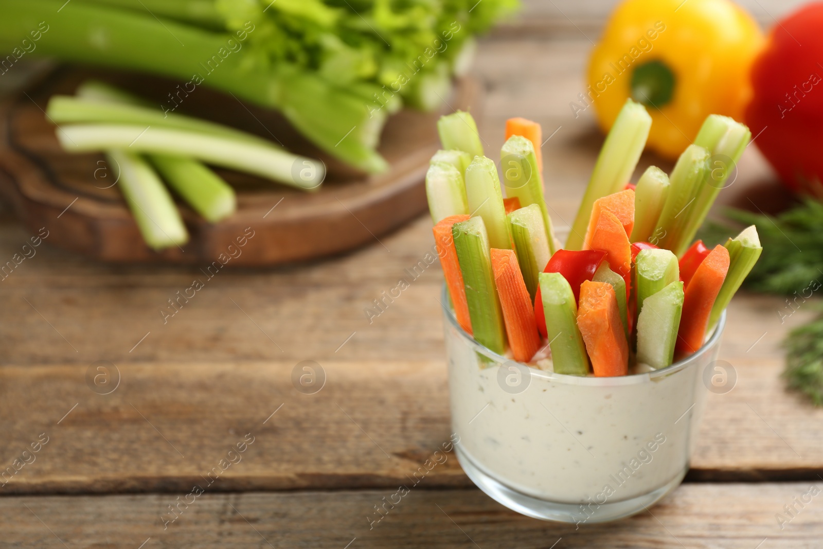 Photo of Celery and other vegetable sticks with dip sauce in glass bowl on wooden table. Space for text