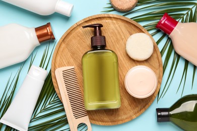 Photo of Shampoo bottles, wooden comb, hair and face masks, solid shampoo bars and palm leaves on turquoise background, flat lay