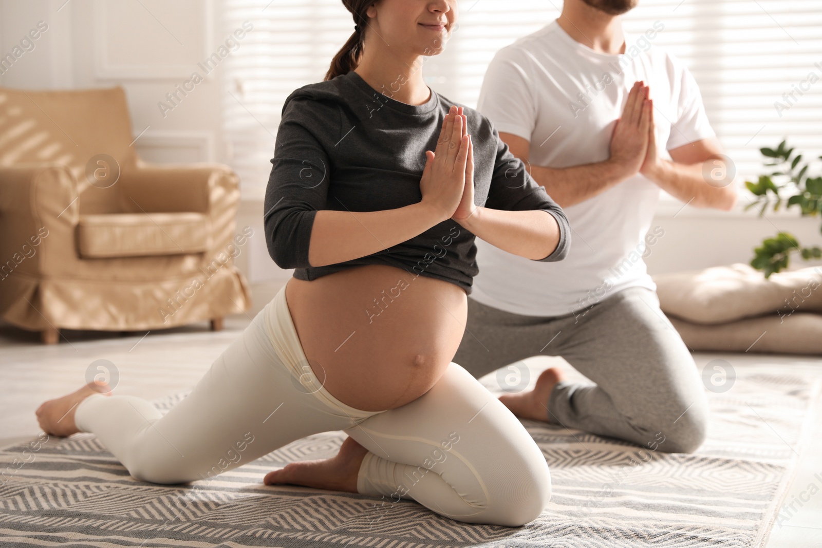 Photo of Young pregnant woman with her husband practicing yoga at home, closeup