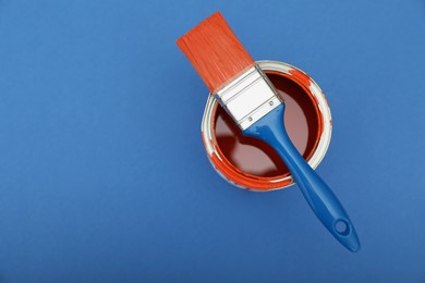 Photo of Can of orange paint and brush on blue background, top view. Space for text