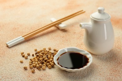Photo of Soy sauce in bowl and beans on beige textured table
