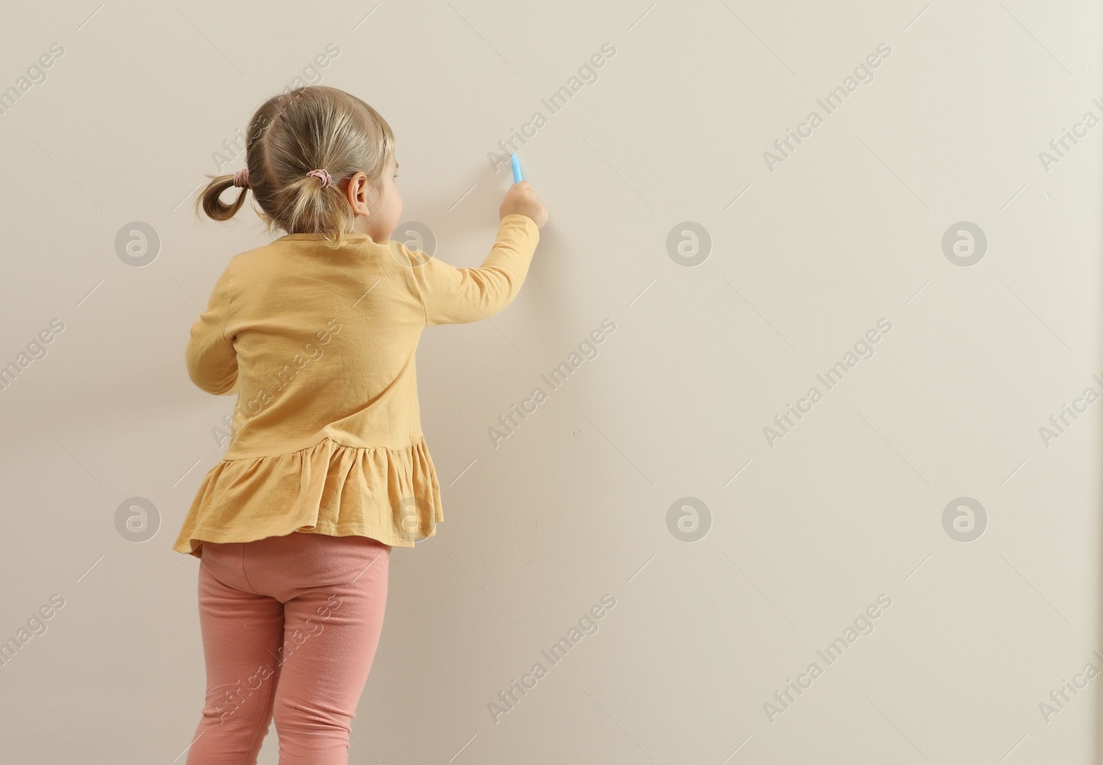Photo of Little girl drawing on beige wall, back view and space for text. Child`s art
