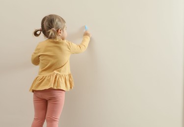 Photo of Little girl drawing on beige wall, back view and space for text. Child`s art